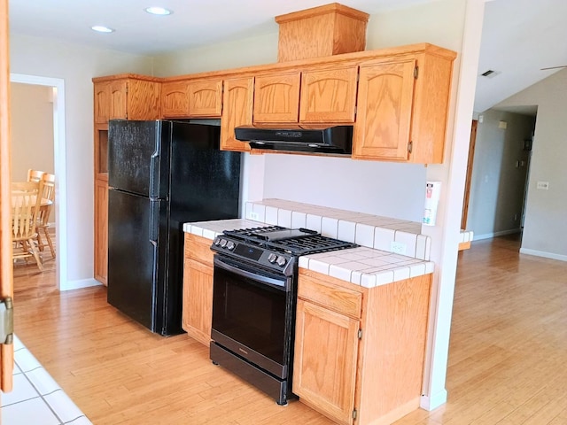 kitchen featuring black refrigerator, tile counters, light wood-type flooring, and stainless steel gas stove