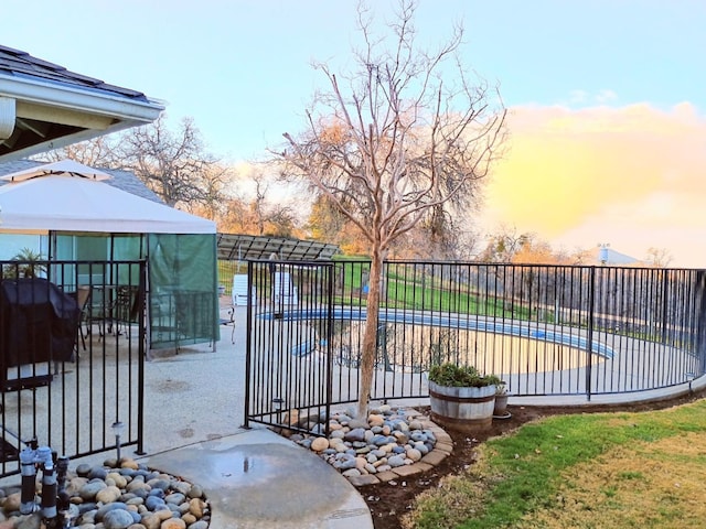 gate at dusk featuring a gazebo and a covered pool