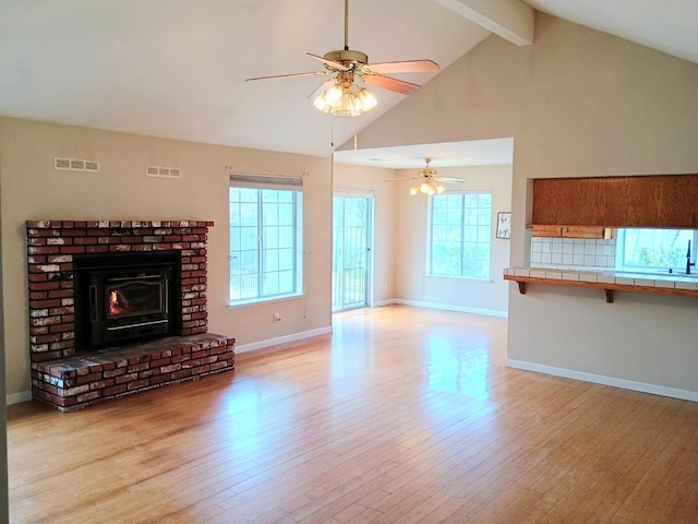 unfurnished living room with ceiling fan, beam ceiling, high vaulted ceiling, and light hardwood / wood-style flooring