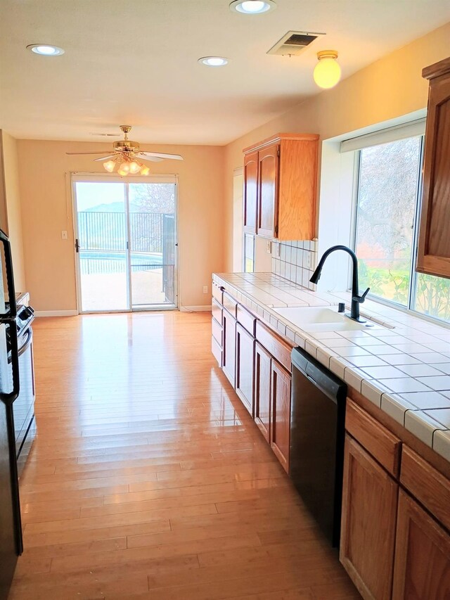 kitchen featuring visible vents, dishwasher, a sink, a ceiling fan, and tile countertops
