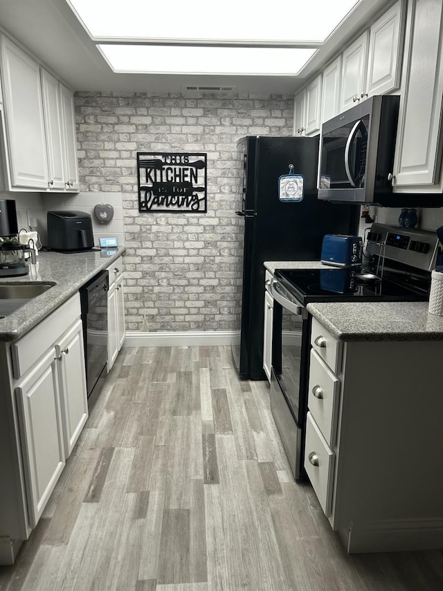 kitchen featuring brick wall, dishwasher, white cabinetry, light hardwood / wood-style floors, and stainless steel electric range