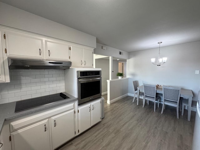 kitchen featuring white cabinetry, black electric stovetop, decorative backsplash, hanging light fixtures, and stainless steel oven