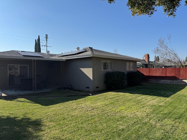 rear view of house featuring a patio, a lawn, and solar panels