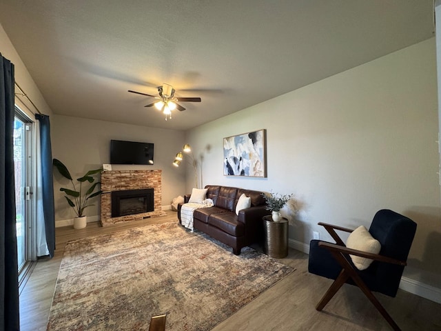 living room with ceiling fan, a stone fireplace, and light hardwood / wood-style floors