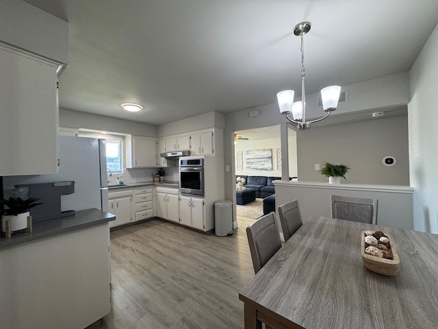 kitchen featuring pendant lighting, white cabinets, backsplash, a notable chandelier, and stainless steel oven