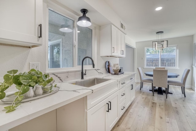 kitchen featuring white cabinetry, sink, light hardwood / wood-style flooring, pendant lighting, and light stone counters