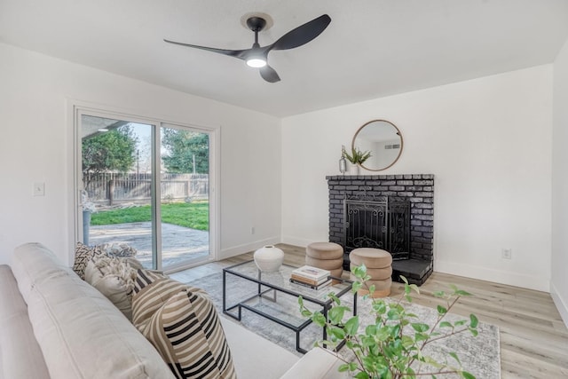 living room featuring a brick fireplace, ceiling fan, and light wood-type flooring