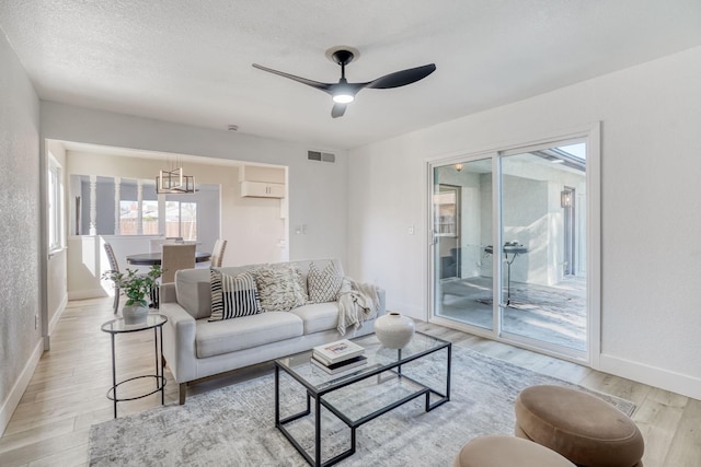 living room featuring ceiling fan, a textured ceiling, and light wood-type flooring