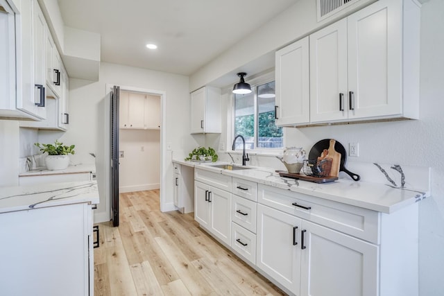 kitchen with sink, light wood-type flooring, white cabinetry, and light stone counters