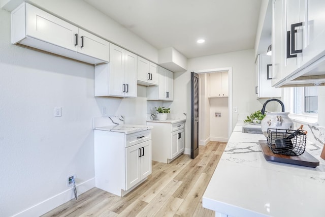 kitchen with white cabinets, light wood-type flooring, light stone countertops, and sink