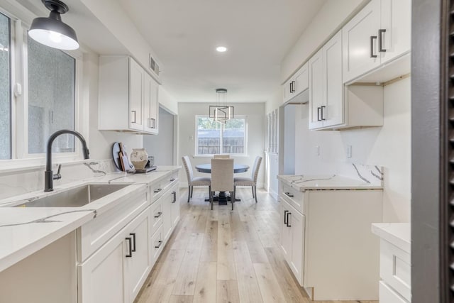 kitchen with light hardwood / wood-style floors, light stone counters, white cabinetry, and decorative light fixtures