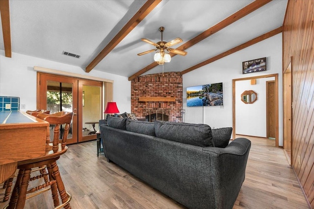 living room with light hardwood / wood-style floors, a brick fireplace, french doors, vaulted ceiling with beams, and wood walls