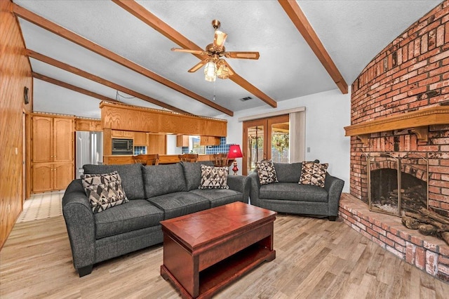 living room with ceiling fan, light hardwood / wood-style flooring, a fireplace, and lofted ceiling with beams