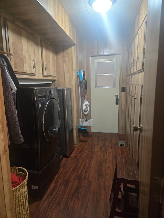 laundry area featuring dark hardwood / wood-style flooring, wooden walls, washer / clothes dryer, and cabinets