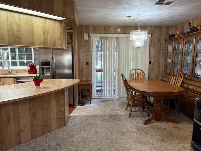 carpeted dining space with sink, a chandelier, and wooden walls