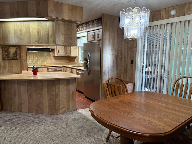 kitchen featuring appliances with stainless steel finishes, sink, an inviting chandelier, backsplash, and wood walls