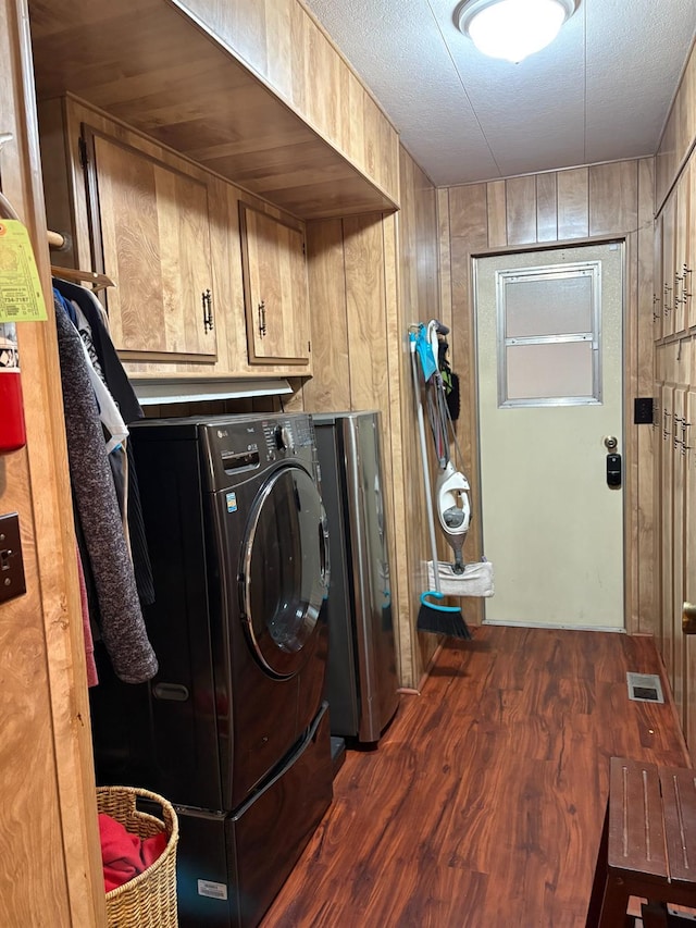 clothes washing area with wood walls, cabinets, dark wood-type flooring, and washer / clothes dryer