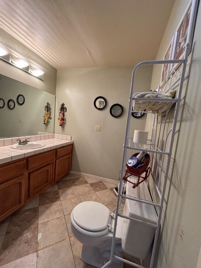 bathroom with baseboards, a textured ceiling, toilet, and vanity