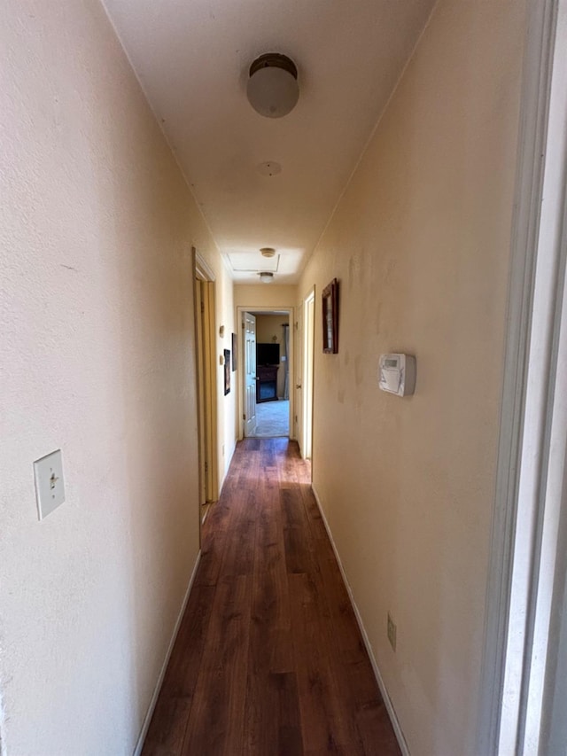 corridor featuring baseboards and dark wood-type flooring