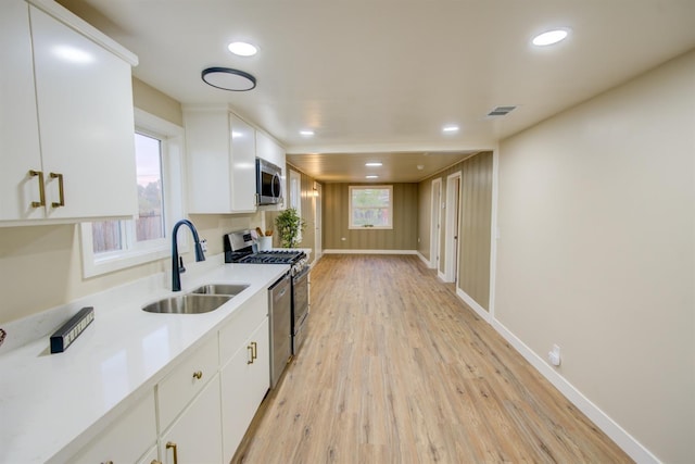 kitchen with sink, white cabinets, light wood-type flooring, and stainless steel appliances