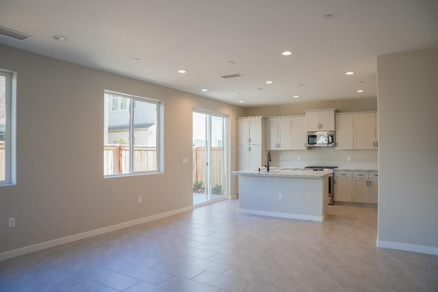 kitchen featuring sink, white cabinets, light tile patterned floors, a center island with sink, and stainless steel appliances