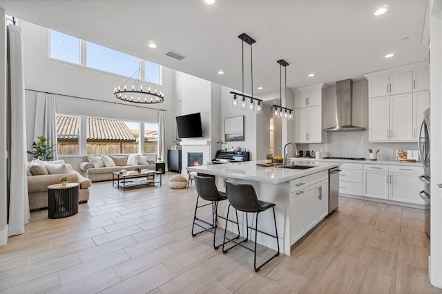 kitchen with wall chimney range hood, white cabinetry, a center island with sink, and sink