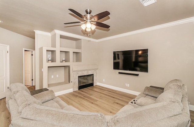 living room with crown molding, hardwood / wood-style flooring, built in features, a premium fireplace, and ceiling fan