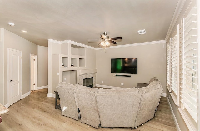 living room with crown molding, built in features, ceiling fan, and light wood-type flooring