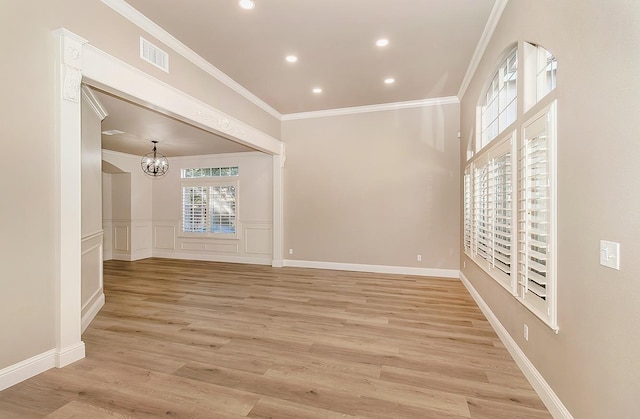 empty room with ornamental molding, a notable chandelier, and light hardwood / wood-style floors