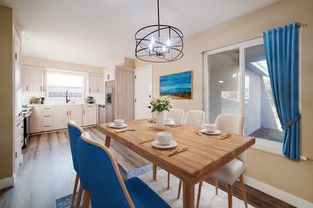 dining space with light wood-type flooring, a healthy amount of sunlight, a notable chandelier, and sink