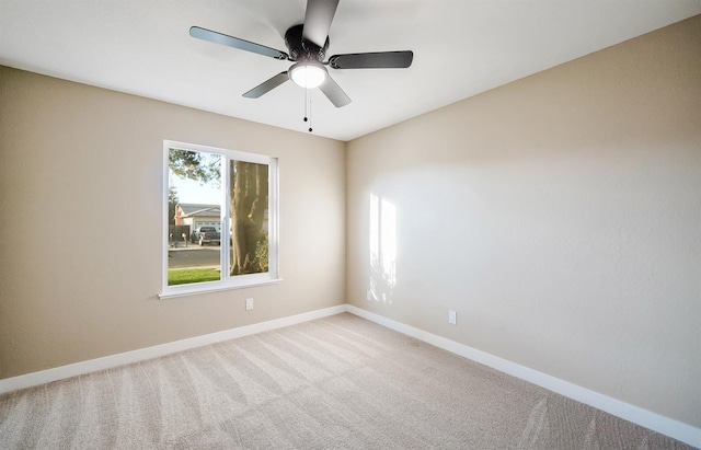 carpeted spare room featuring baseboards and a ceiling fan