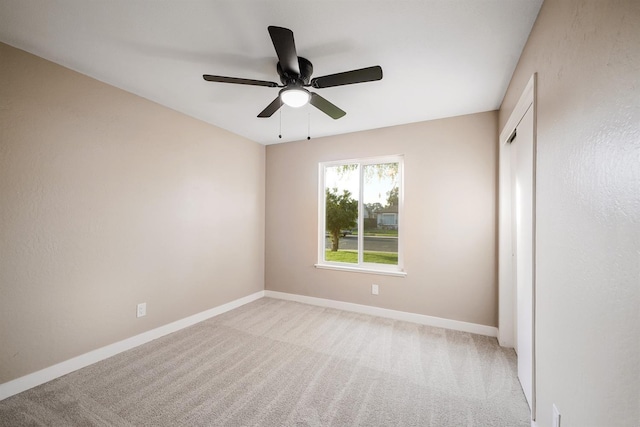 spare room featuring a ceiling fan, light colored carpet, and baseboards