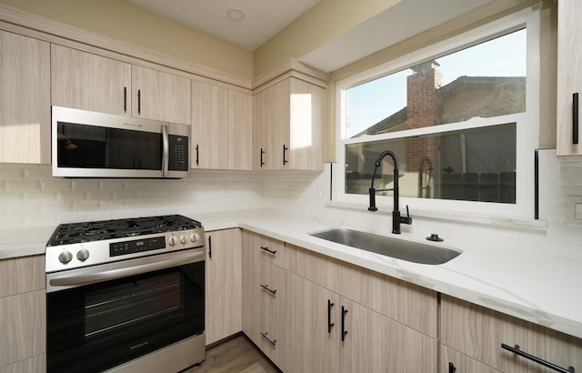 kitchen with light brown cabinetry, appliances with stainless steel finishes, a sink, and decorative backsplash