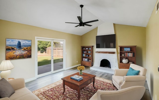 living area with lofted ceiling, a brick fireplace, light wood-type flooring, and a ceiling fan