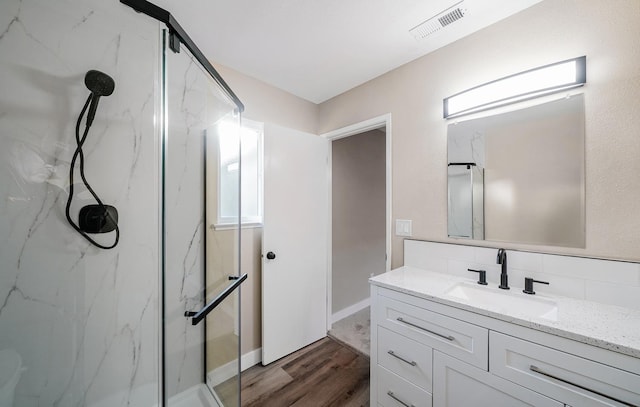 bathroom with a marble finish shower, visible vents, backsplash, vanity, and wood finished floors