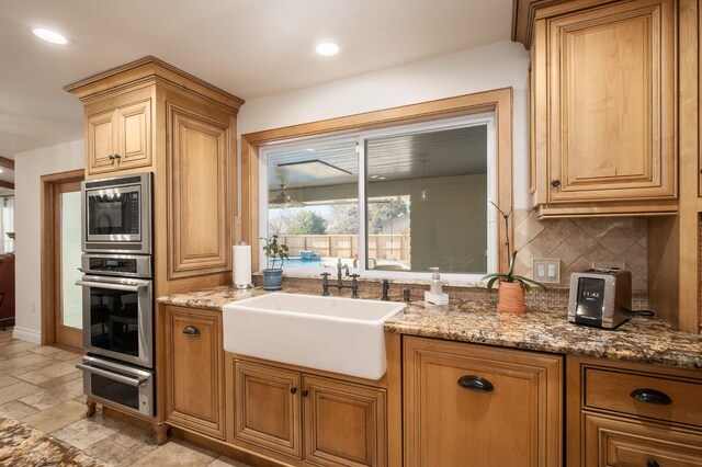 kitchen with backsplash, appliances with stainless steel finishes, sink, and stone counters