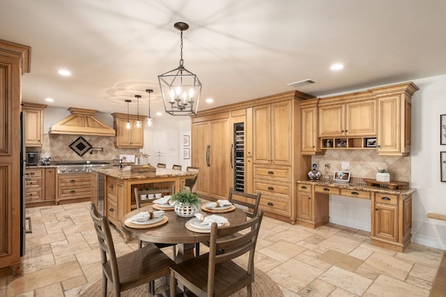 kitchen with premium range hood, decorative light fixtures, light stone countertops, a kitchen island with sink, and backsplash