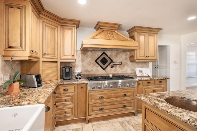 kitchen with sink, backsplash, light stone counters, custom exhaust hood, and stainless steel gas stovetop