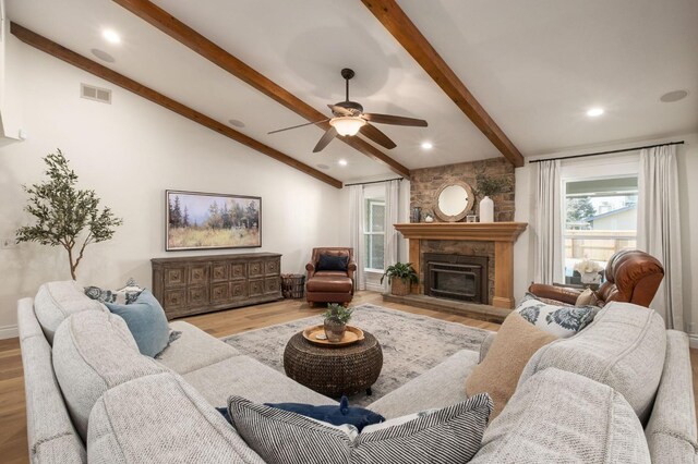 living room featuring vaulted ceiling with beams, a stone fireplace, light hardwood / wood-style flooring, and ceiling fan