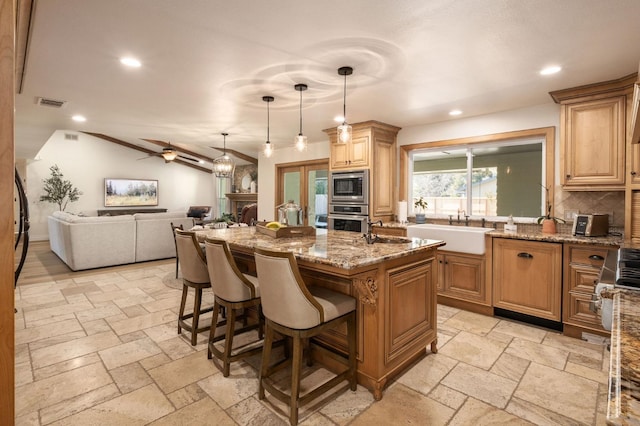 kitchen featuring sink, stone counters, hanging light fixtures, stainless steel appliances, and an island with sink