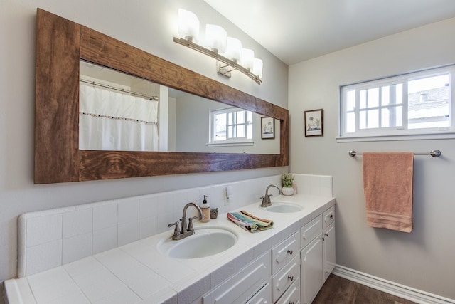 bathroom featuring wood finished floors, a sink, baseboards, and double vanity