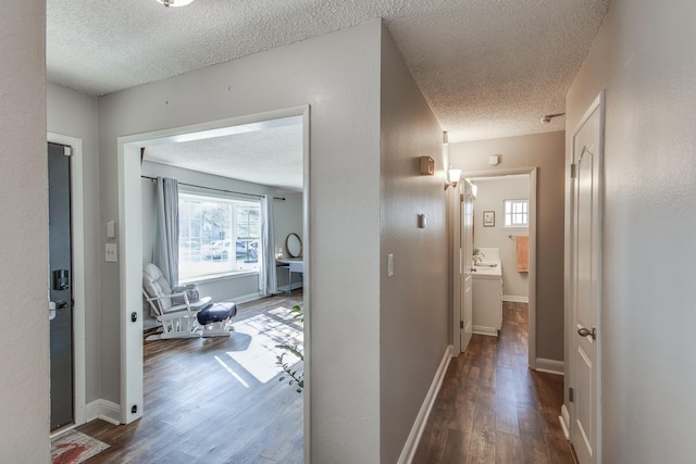 hallway with a textured ceiling, baseboards, and wood finished floors