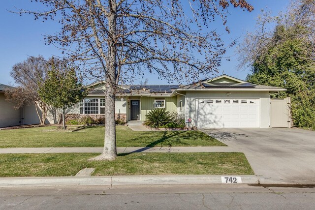 ranch-style home featuring a garage, a front yard, and solar panels