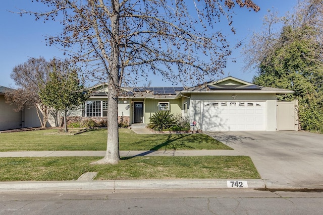 single story home featuring solar panels, concrete driveway, a front lawn, and an attached garage