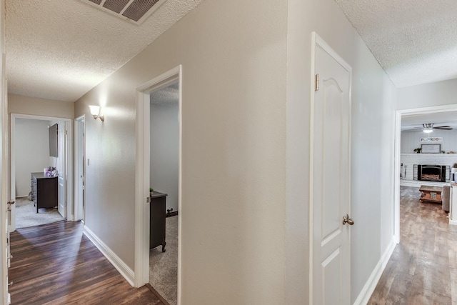 hallway featuring visible vents, a textured ceiling, baseboards, and wood finished floors