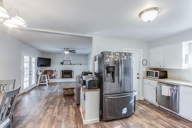 kitchen with a brick fireplace, white cabinetry, stainless steel appliances, and wood finished floors