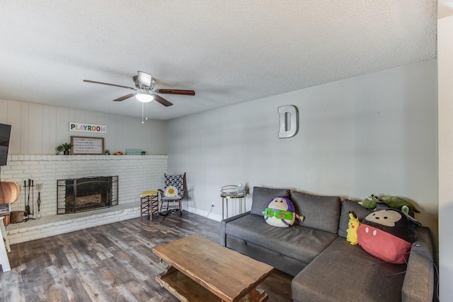 living area featuring a textured ceiling, ceiling fan, a fireplace, wood finished floors, and baseboards