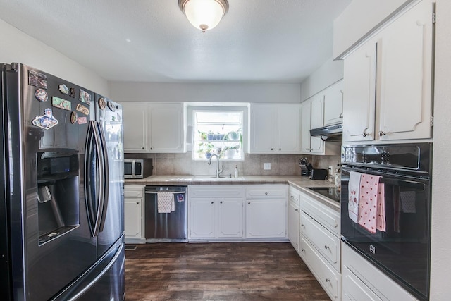 kitchen with under cabinet range hood, dark wood-type flooring, a sink, backsplash, and black appliances