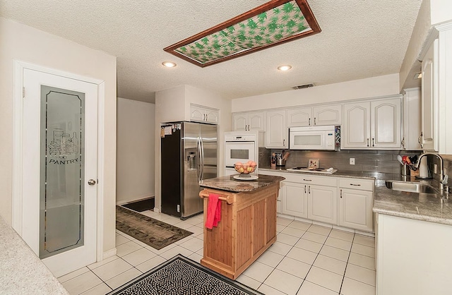 kitchen featuring sink, a center island, a textured ceiling, white appliances, and white cabinets