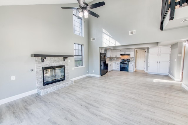 unfurnished living room featuring a brick fireplace, a towering ceiling, ceiling fan, and light wood-type flooring